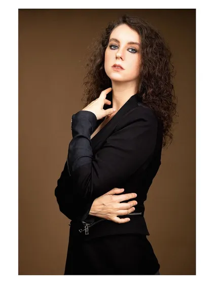 A powerful and elegant portrait of a model in a black blazer against a warm brown background.