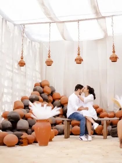A cozy and intimate pre-wedding moment. The couple, dressed in white, shares a quiet embrace in a beautifully rustic setting with earthen pots.