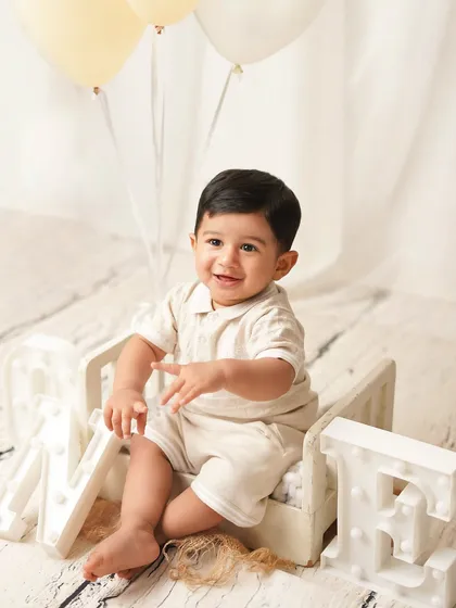 The one-year-old sits in a miniature bed next to 'ONE' marquee letters. He's clapping his hands, full of excitement for his big day.