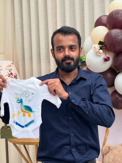 A guest proudly holds up the dinosaur-themed onesie he painted. It's a fun and personal gift that the parents will love.