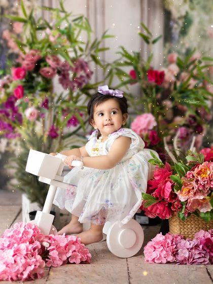 A sweet girl on her tricycle, surrounded by a garden of pink flowers. This whimsical setup is perfect for a magical and feminine photoshoot.