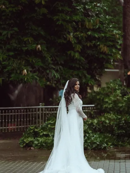 The bride's gown and long veil create a dramatic and beautiful silhouette against the lush greenery. This is a moment of pure bridal elegance, expertly captured.