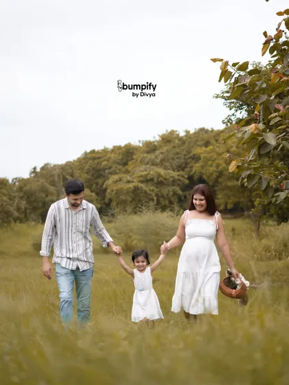 The family of three walks hand-in-hand through the tall grass, with their daughter in the middle, excited about her new role as a big sister. A perfect family maternity portrait.