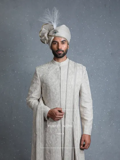 A closer look at the ivory jacquard sherwani, showcasing the texture and the graceful drape of the matching stole. The feather-adorned turban completes this portrait of regal elegance.