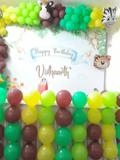 A full view of our jungle theme birthday backdrop for Vidhaarth's second birthday. The setup includes a personalized banner, animal character foil balloons, and a vibrant balloon arrangement in green, yellow, and brown.