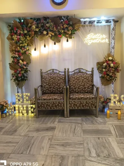 A cozy engagement decoration for a home party. The setup includes a floral corner arch, a "Better Together" neon sign, and light-up "Be Mine" letters for a romantic touch.