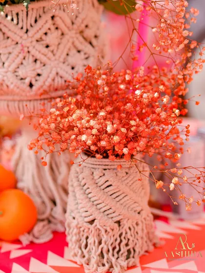A detail shot of a macrame-wrapped vase holding delicate orange baby's breath, showcasing the event's bohemian-chic aesthetic.