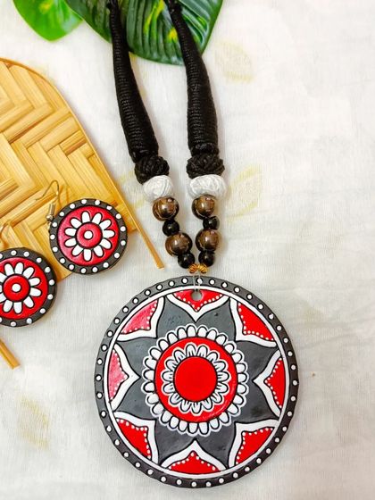 A sleek and beautiful terracotta necklace with a large, circular mandala pendant in red, gray, and black.