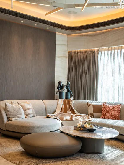 At the prestigious Lodha Worldview Apartments, this luxe residence embodies understated sophistication. The living room's design is enhanced by the apartment's natural curves, creating a seamless flow between spaces, with warm, recessed lighting adding to the ambiance.