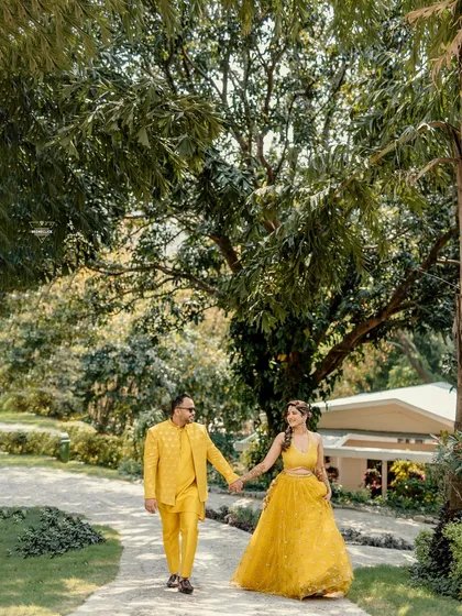The couple walking hand-in-hand through a beautiful garden path, their matching yellow outfits shining in the sun.