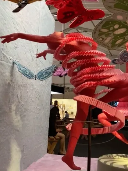 A dynamic paper sculpture of a dancer from the 'We/Us' installation. The figure is caught mid-movement, its form unraveling into a spiral of pleated paper.