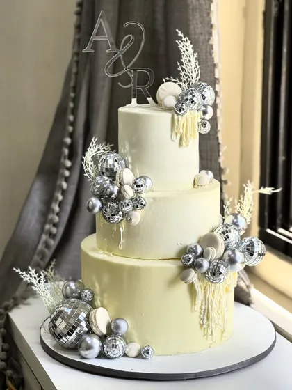 Glamour was the theme for this stunning three-tiered celebration cake. Adorned with sparkling silver disco balls and custom initials, it’s a showstopper designed to make any grand event unforgettable.