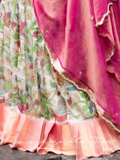 Detail of the hand-painted Kalamkari skirt, featuring intricate floral and bird motifs. The pink tissue georgette dupatta adds a soft, contrasting layer.