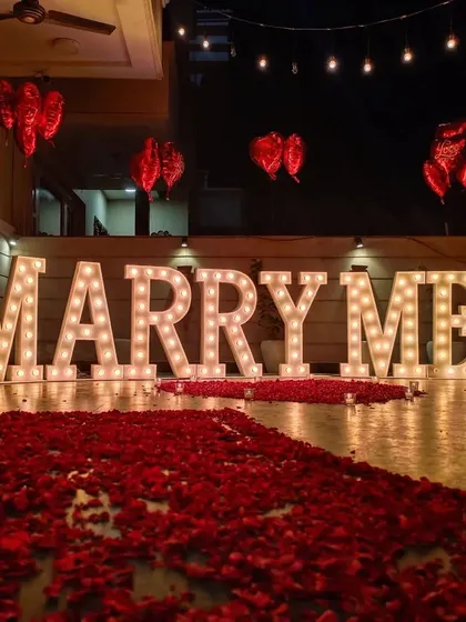 A classic terrace proposal decoration featuring our large marquee 'MARRY ME' letters. We created a dramatic entrance with a long path of red rose petals, leading up to the main display.