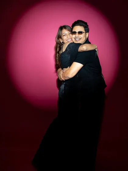 A warm, candid hug captured in the studio. The spotlight effect on the pink background creates an intimate circle of light around the couple, emphasizing their joyful embrace and genuine affection in this pre-wedding portrait.