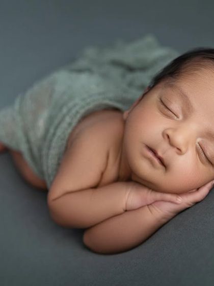 A peaceful side lying pose, showing the baby's profile and soft cheeks. The simple grey wrap and background create a modern, timeless look.