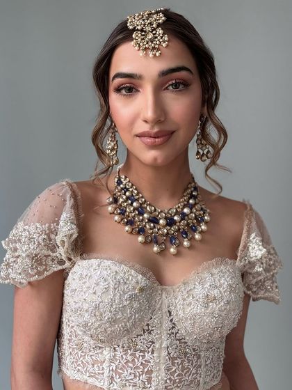 A modern take on a bridal updo. This textured, messy bun is accented with a stunning gold and pearl hair accessory, making it a perfect style for a contemporary bride's reception or cocktail event.