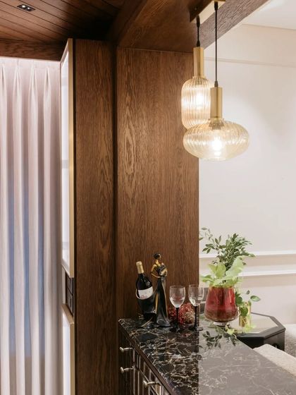 This bar and storage unit, framed by rich wood, adds a touch of sophistication to the living area. The warm pendant lights and dark marble countertop make it a perfect spot for evening entertainment.