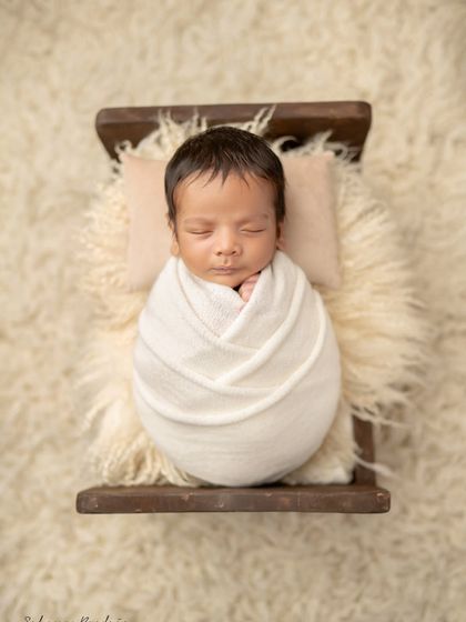 A classic portrait of a swaddled newborn, resting peacefully on a tiny bed. These are the timeless images you will cherish forever.