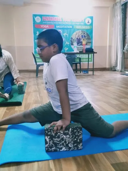 A young student works on his front splits with the help of a yoga block and wall support. We encourage a gradual and safe approach to increasing flexibility at any age.