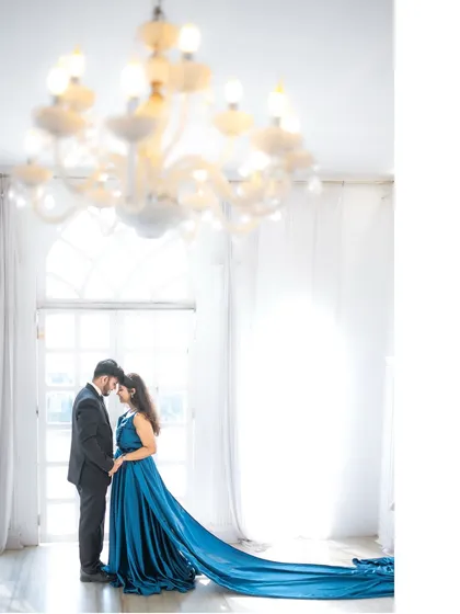 An artistic silhouette of a couple in a beautiful, high-ceilinged room with a chandelier, the bride's long blue train creating a sweeping visual effect. This shot emphasizes elegance and drama.