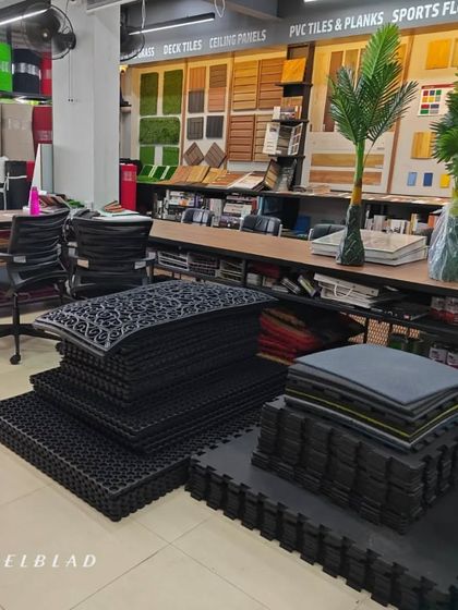 A section of our showroom displaying various flooring and matting solutions, including interlocking gym tiles and cushion mats, with our paneling samples in the background.