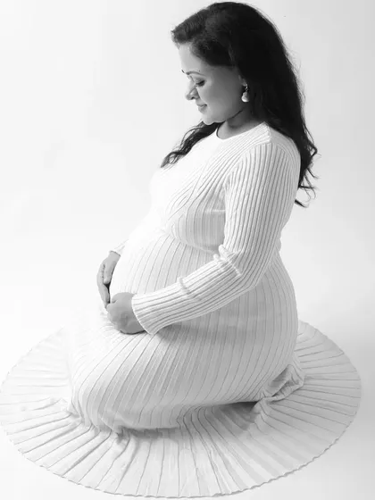 A serene and elegant black and white portrait of a mother to be. Kneeling gracefully, she cradles her bump, creating a timeless image of maternal love.