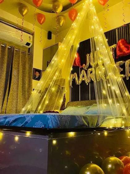 Perfect for newlyweds, this "Just Married" room setup features a beautiful canopy over the bed illuminated with warm fairy lights, with gold and red balloons adding to the celebratory feel.