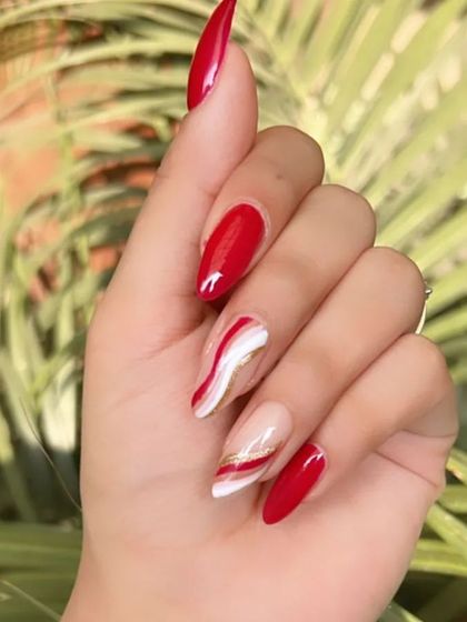 A striking set of almond-shaped nails with a mix of solid bright red and accent nails with red, white, and gold waves.