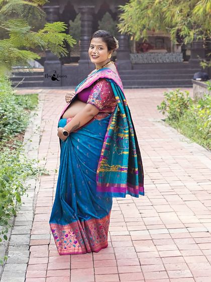 A radiant smile from the mother-to-be. Dressed in a stunning blue and pink Paithani saree, she looks absolutely beautiful against the lush green backdrop.