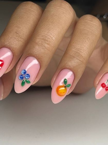 A cute and playful 3D fruit-themed nail art set. Each nail is adorned with a different sculpted fruit, including a mushroom, blueberries, an orange, and cherries, on a sweet pink base.