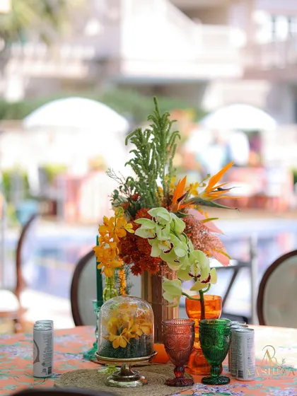A full view of the tropical centerpiece, featuring birds of paradise, orchids, and other colorful blooms, complemented by fresh oranges and bold glassware.