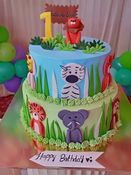 A colorful two-tiered jungle theme cake for a first birthday. The sides are decorated with cute, flat-design jungle animals.
