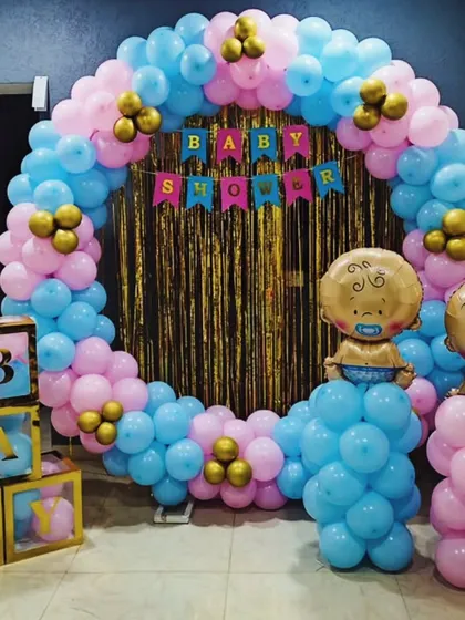 Celebrating with a splash of color. This baby shower setup is perfect for a gender reveal, with a full balloon ring in pink and blue, a sparkling gold backdrop, and cute baby-themed props to make the moment pop. 🎈
