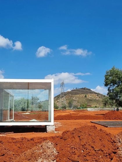 The very beginning of a new project. The site is a blank canvas of red earth, with a simple glass structure offering a view of the surrounding hills. This is where the process of ecological planning and master design begins.