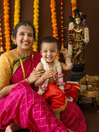 A joyful mother and son portrait. The baby, dressed as Krishna, holds onto a statue of the deity, creating a wonderful connection between theme and subject.