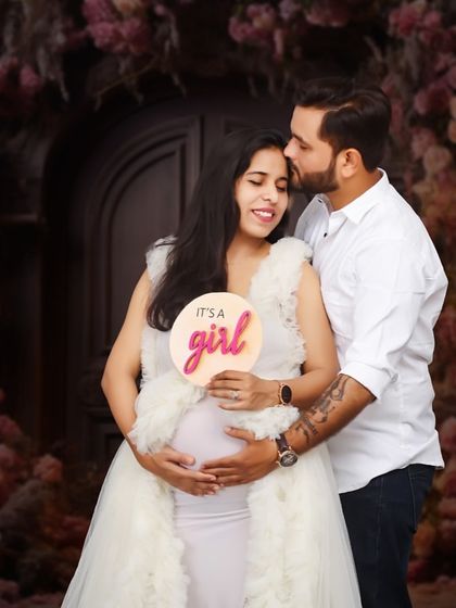 It's a girl! A joyful studio portrait where the couple announces the gender of their baby with a cute sign, surrounded by a beautiful floral backdrop.