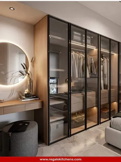 We integrated a full vanity table into this wardrobe design, complete with a lit circular mirror. The glass doors offer a peek at the organized interior, blending functionality and style.