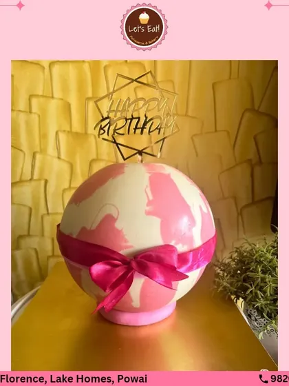 A surprise-inside piñata cake. This chocolate sphere, decorated with a pink ribbon, is designed to be broken open to reveal a hidden stash of treats, adding an element of fun to the celebration.