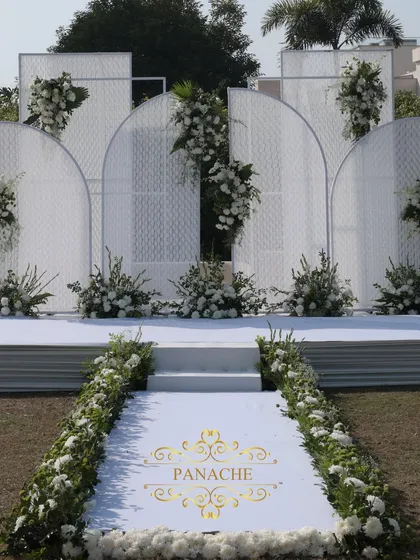 The stunning all-white stage, featuring modern arched panels and asymmetrical floral arrangements. It's a perfect example of contemporary and elegant event design.