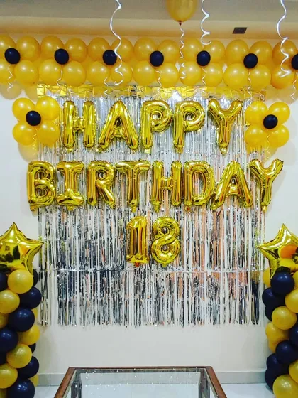 An 18th birthday celebration with a striking yellow and black theme. The decoration features a 'Happy Birthday' foil banner, balloon pillars with star toppers, and a flower-like balloon garland across the top.