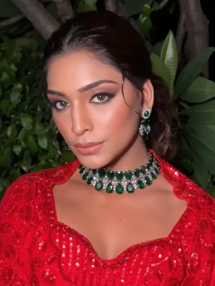 A striking look for a modern reception or cocktail party. The model wears a bold red outfit, perfectly complemented by a choker made of large green stones and sparkling zircons.
