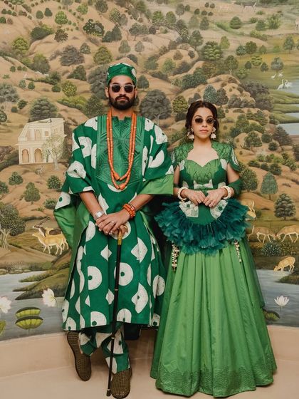 The couple posing against a traditional Indian mural, their modern African-inspired attire creating a beautiful cultural fusion. This image perfectly captures the spirit of 'The Roots' wedding.