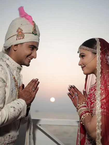 Against the backdrop of a setting sun over the sea, the couple shares a traditional greeting. A unique and serene wedding moment.