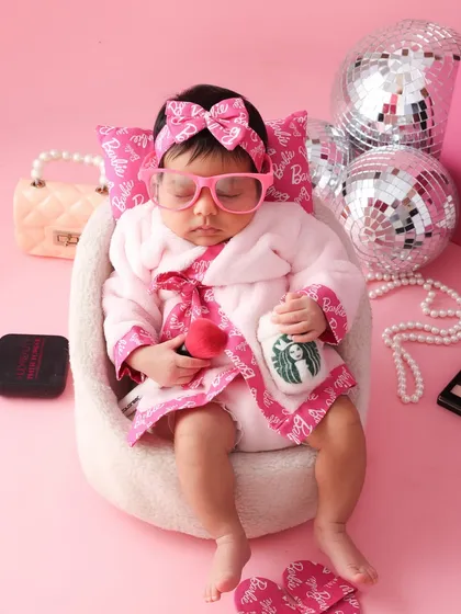 The ultimate Barbie nap. This newborn is styled in a tiny pink bathrobe and sunglasses, looking like a true spa-day Barbie. It’s a hilarious and adorable take on the popular theme.