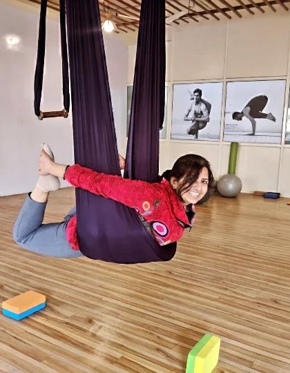 A student enjoys a gentle backbend, Dhanurasana (Bow Pose), while supported by the hammock. This variation makes the pose more accessible and allows for a deep stretch across the chest and shoulders.