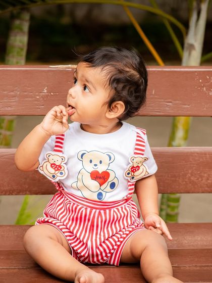 A close-up portrait of a baby boy in an adorable outfit, captured during an outdoor session. The natural light highlights his curious expression.