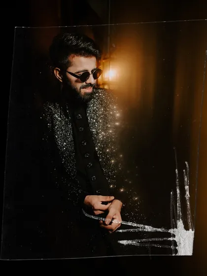 A cool, edgy portrait of the groom in his sparkling Sangeet jacket and sunglasses, captured with an artistic foreground effect.