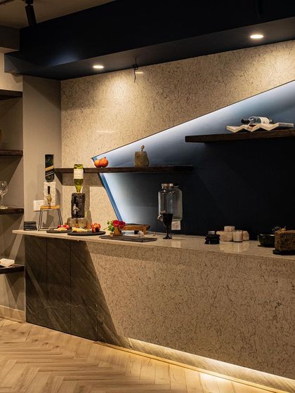 A wider perspective of the custom bar counter, showing how it anchors the space. The angular design, combination of textured and smooth stone, and strategic lighting come together to create a dramatic and welcoming feature.