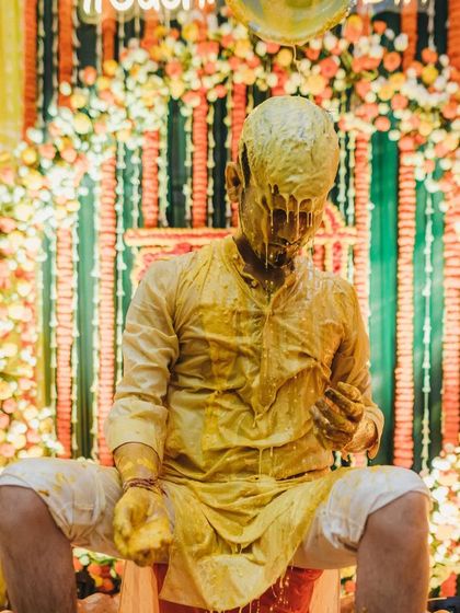 A dramatic shot of the groom completely covered in dripping turmeric paste, a testament to a truly enthusiastic celebration.